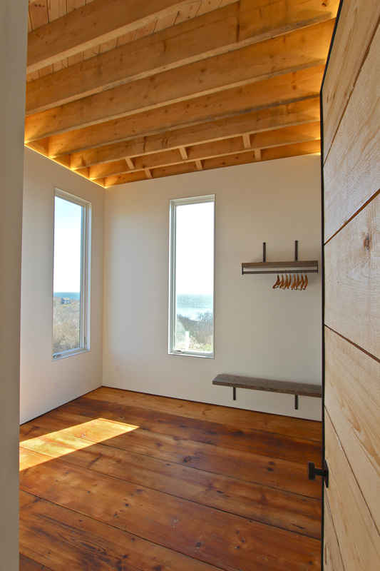 QUARTER design studio + EngineHouse | Seaside Residence | Block Island, RI – master bedroom with exposed ceiling rafters, LED cove lighting, and reclaimed wide-plank flooring (photo provided by EngineHouse)